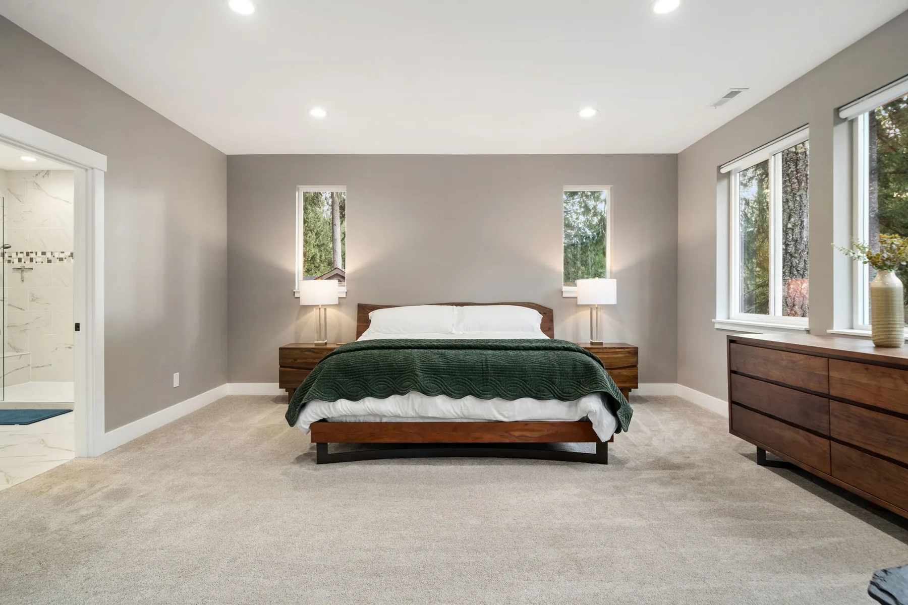 Un dormitorio con una cama centrada, mesas de noche y una cómoda junto a las ventanas.