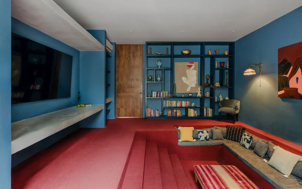 Una sala de estar con paredes azules tiene estantes empotrados y una zona de asientos hundida.