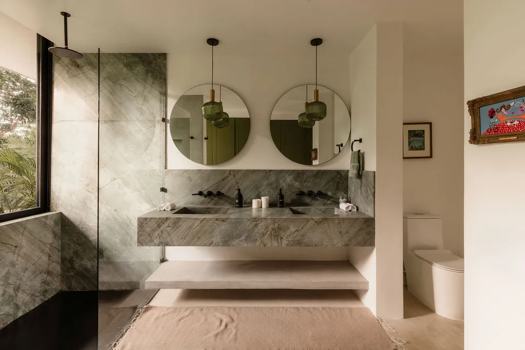 A bathroom with a marble vanity, twin round mirrors, and a separate toilet area.