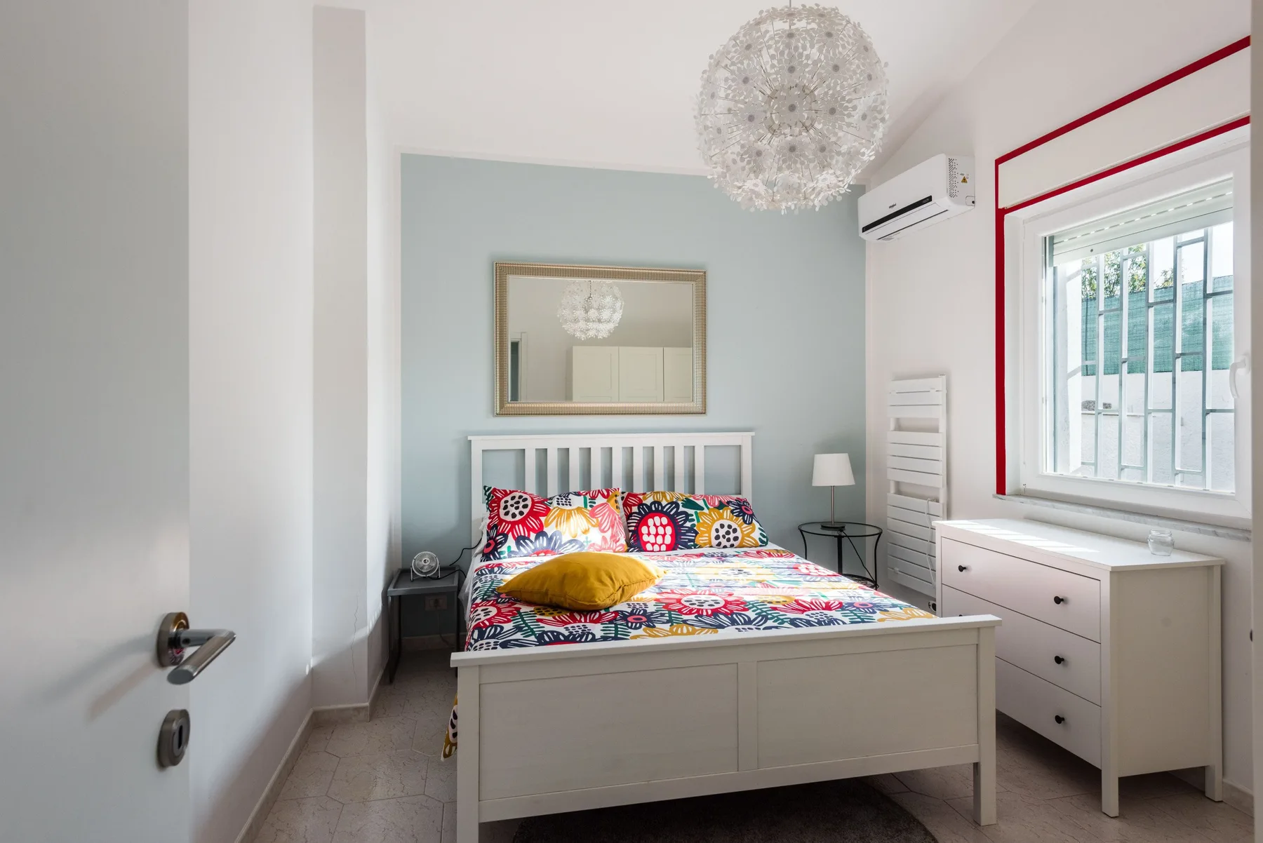 Un dormitorio luminoso con una cama colorida y una ventana grande.