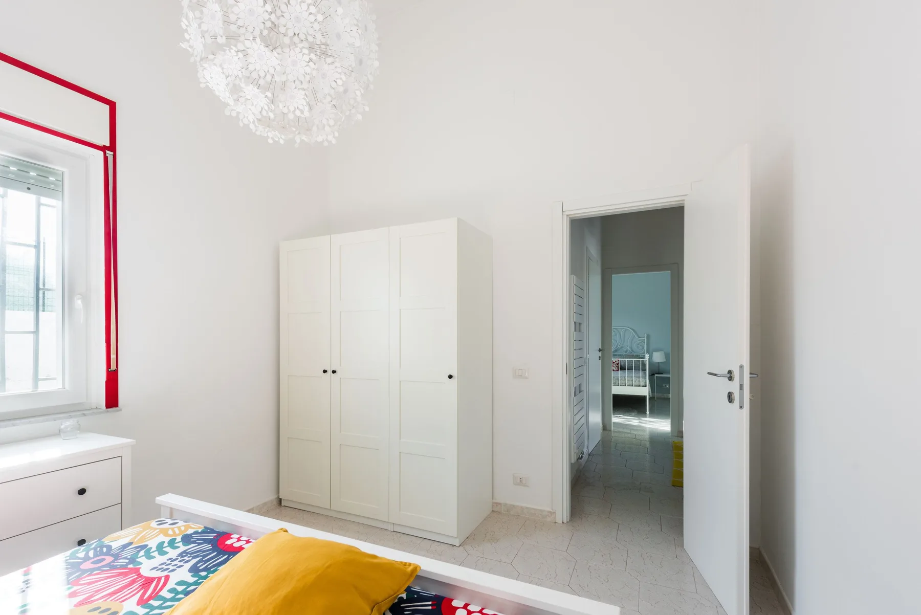 Un dormitorio luminoso con un armario blanco y ropa de cama colorida.