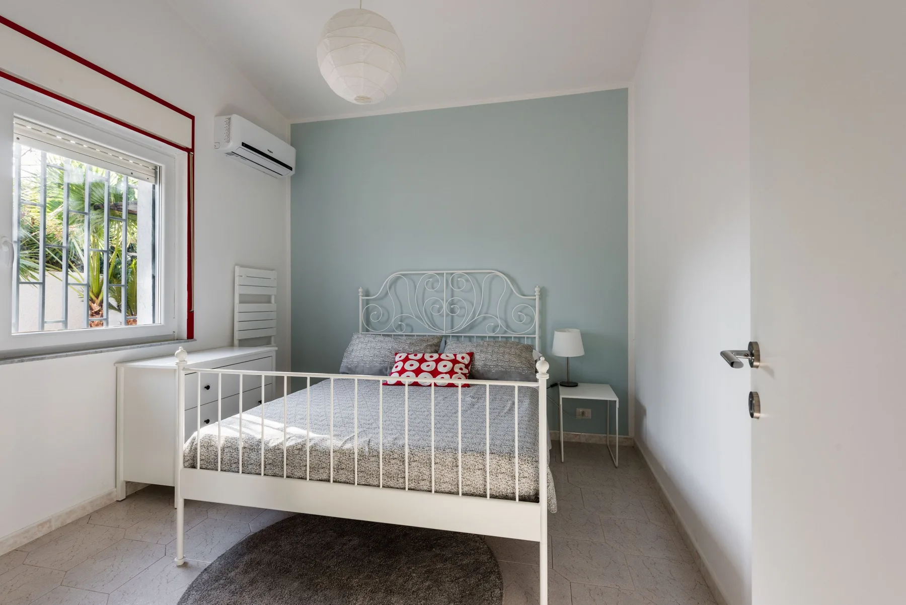 Un dormitorio con una cama blanca, una mesita de noche y una ventana.
