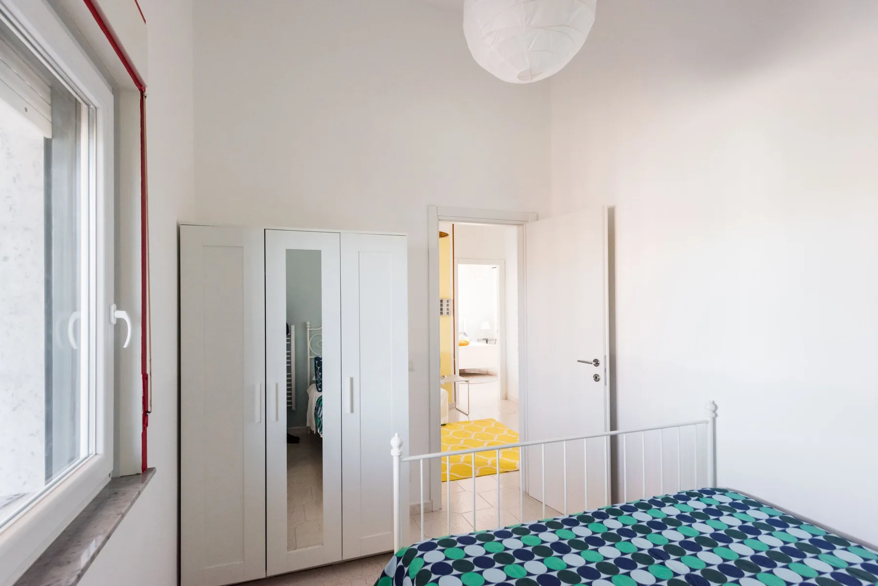 Un dormitorio luminoso con una colcha estampada y un armario abierto.