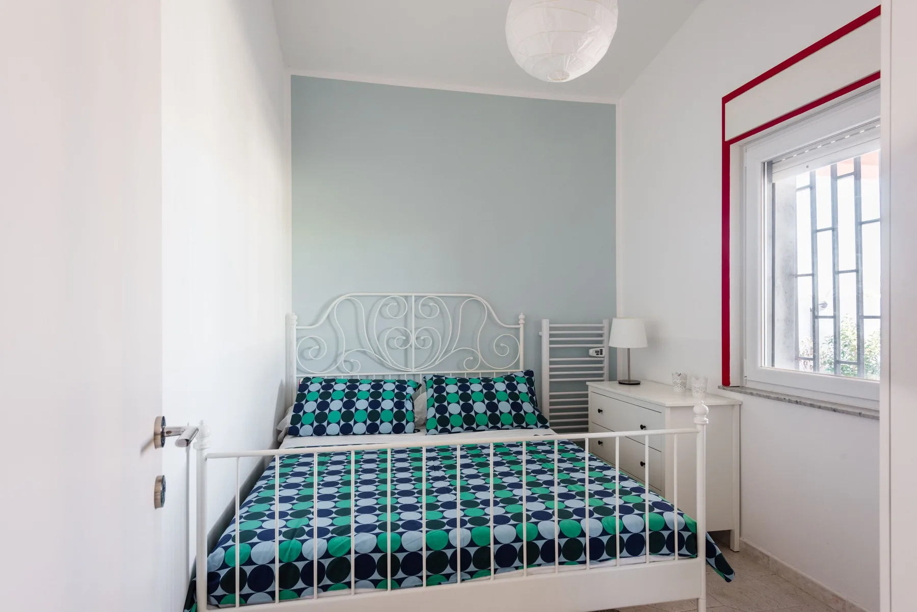 Un dormitorio con una cama blanca cubierta con una colcha estampada en tonos verdes y negros.