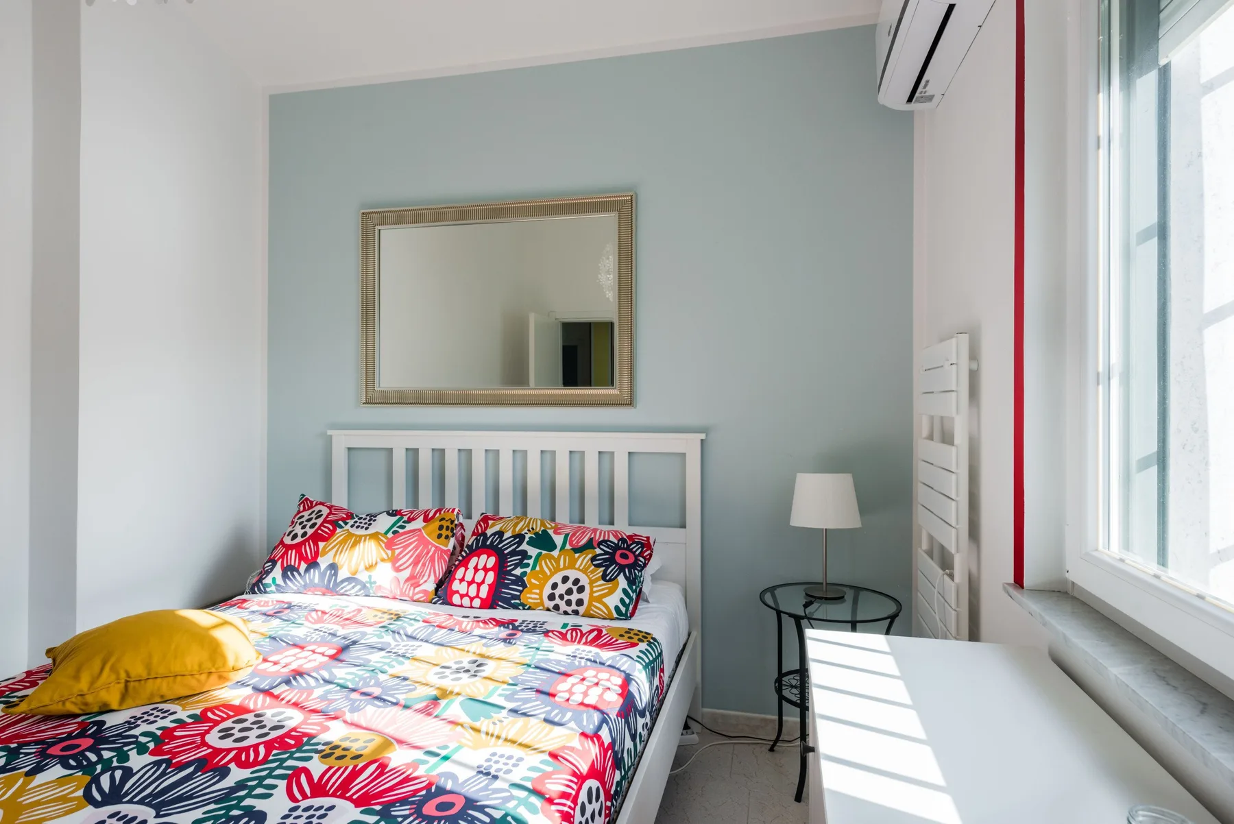 Un dormitorio luminoso con una colcha estampada de colores y una ventana.
