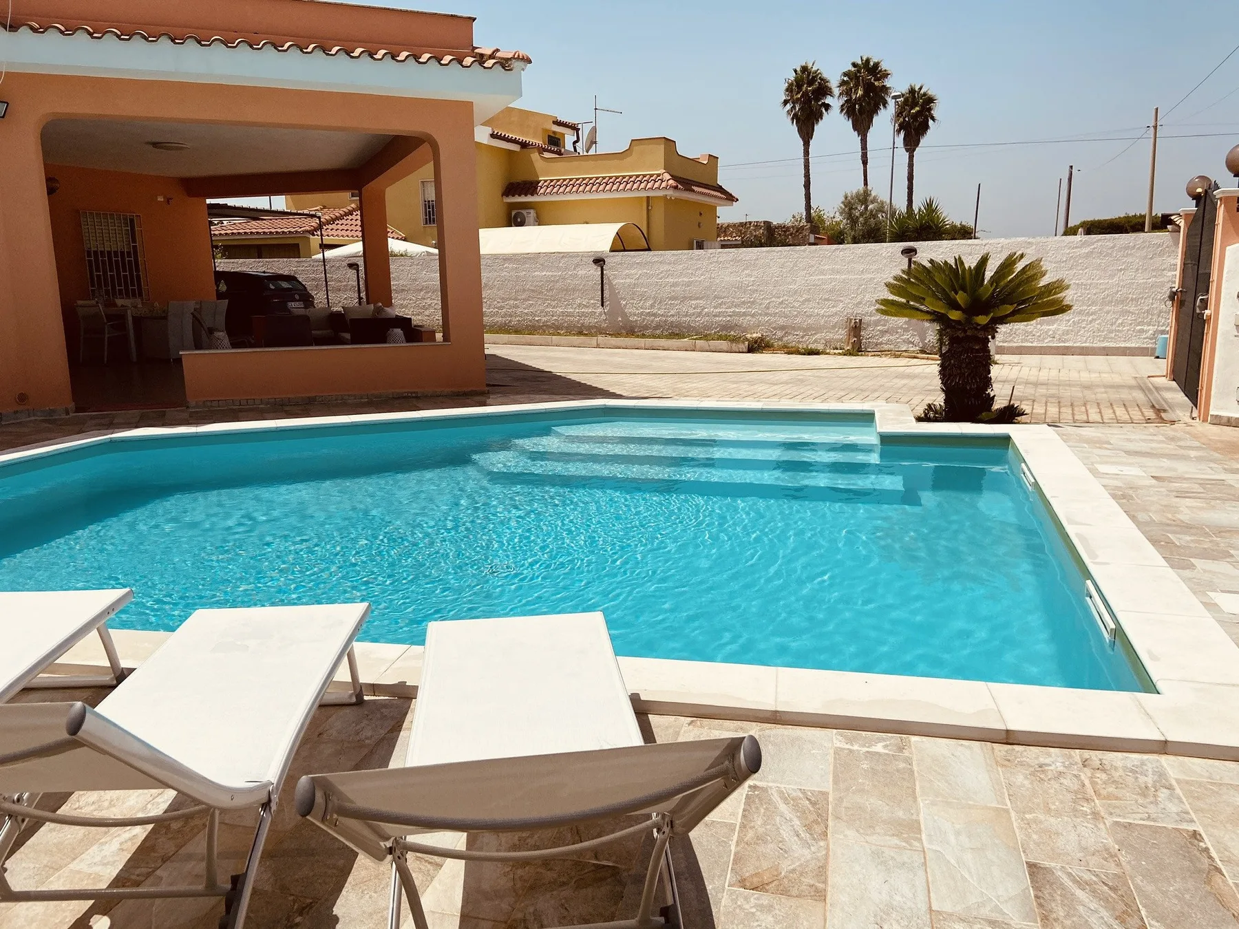 Una piscina junto a un patio sombreado, con tumbonas en el borde.
