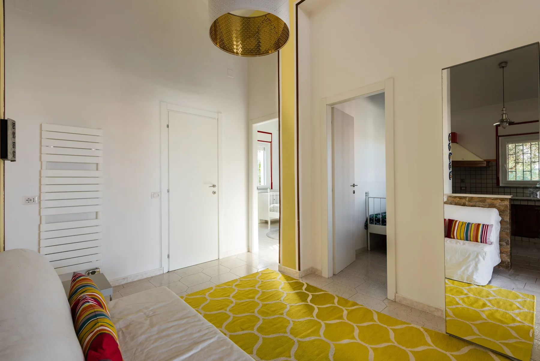 Un dormitorio luminoso con una cama, una alfombra amarilla estampada y una puerta a otra habitación.