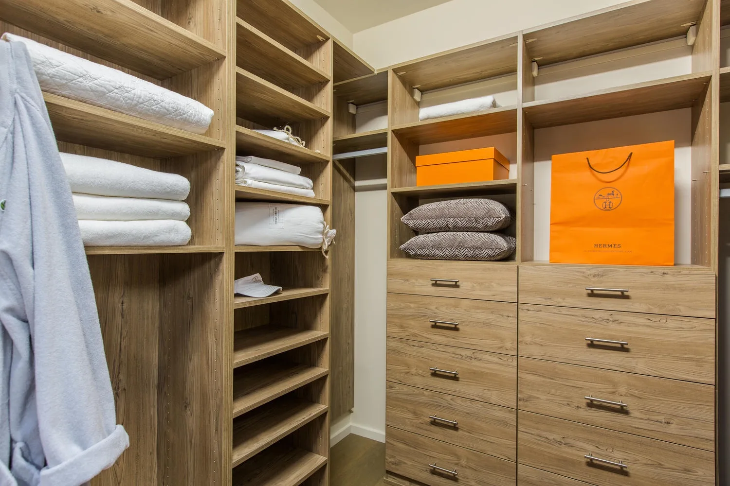 Un vestidor con estantes abiertos, toallas dobladas y cajones de madera.