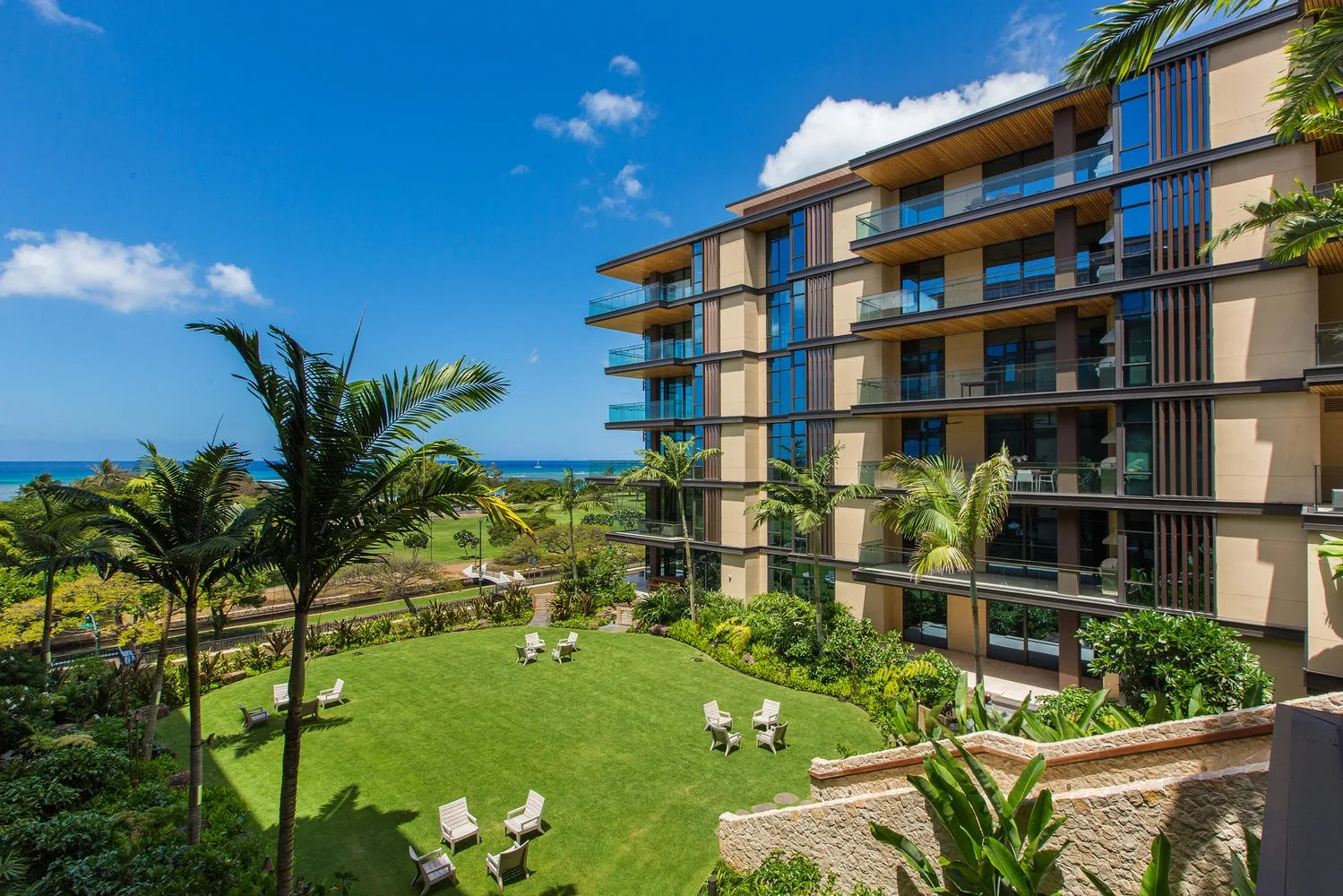 Un jardín ajardinado con asientos junto a un edificio moderno y el océano.