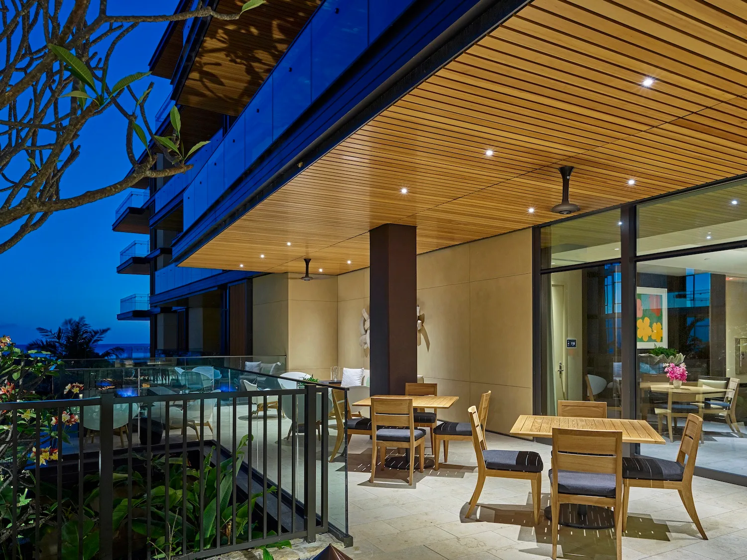 Un patio comedor al aire libre con mesas y asientos bajo un techo revestido de madera.
