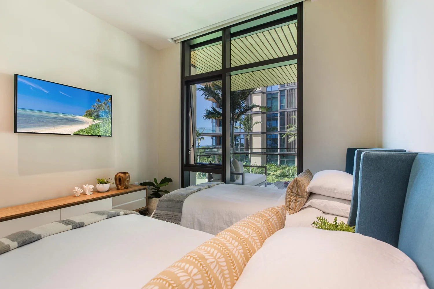 Un dormitorio luminoso con dos camas y una ventana grande con vista a edificios cercanos.