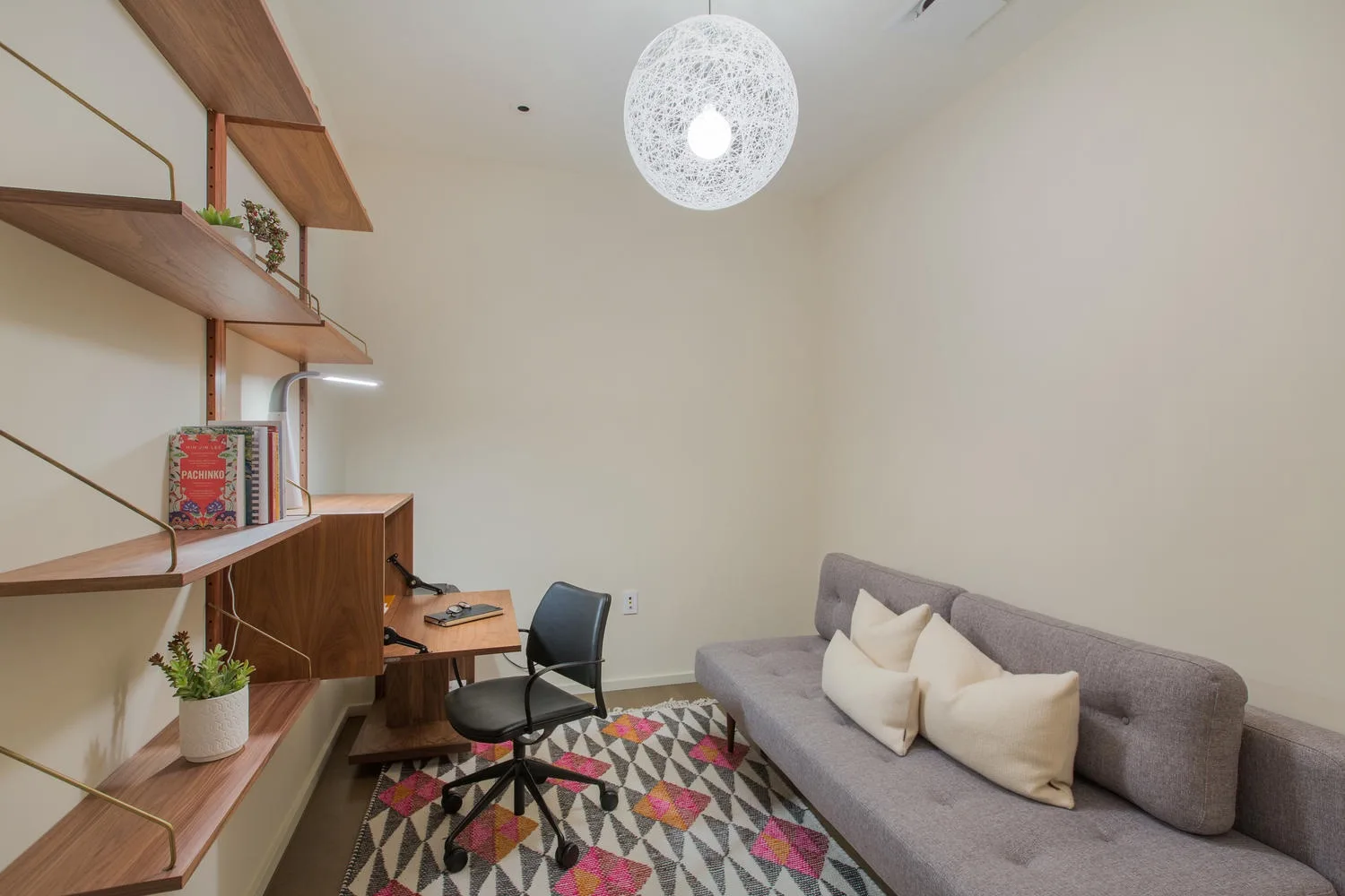 Una sala de estar con sofá gris, alfombra estampada y zona de escritorio.