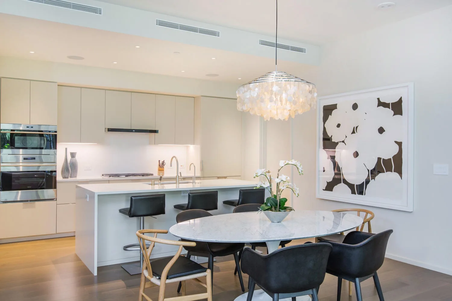 Una cocina y comedor luminosos con mesa, asientos y una lámpara colgante.