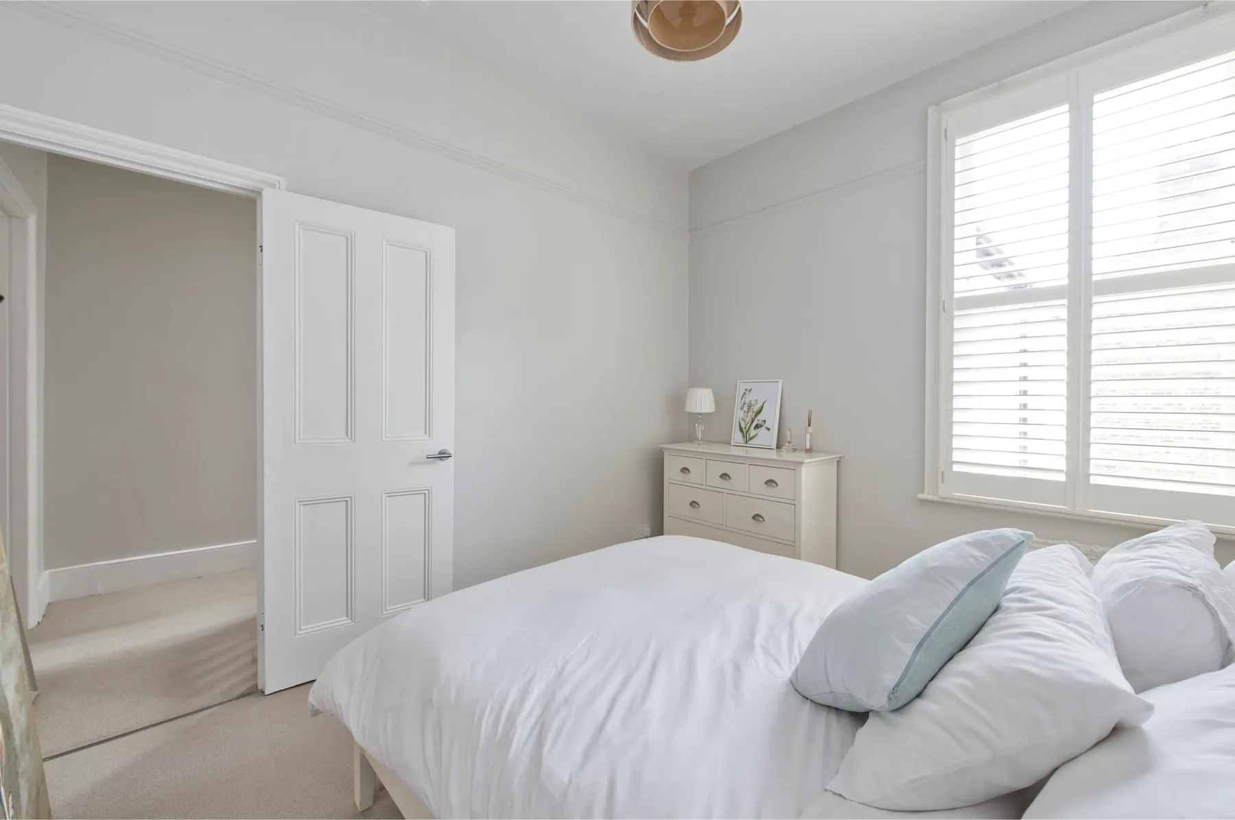 Un dormitorio luminoso con una cama tendida y una cómoda junto a la ventana.