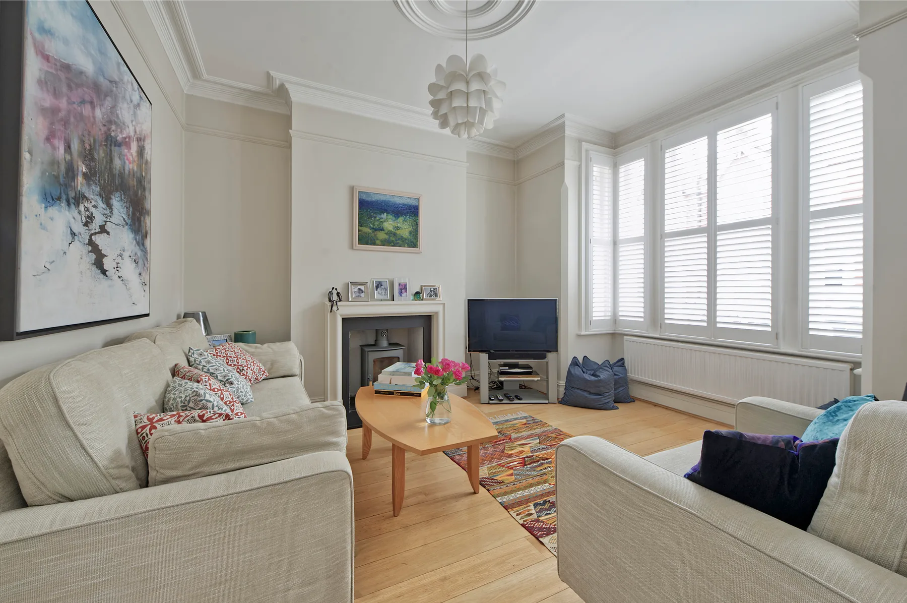 A bright living room with seating, a coffee table, and broad windows with shutters.