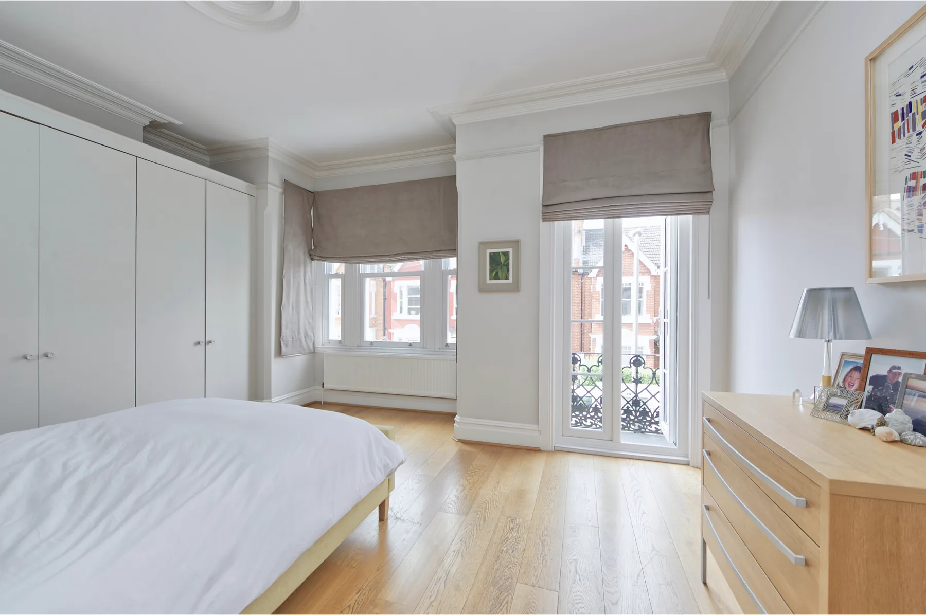 A bright bedroom with a bed, fitted wardrobes, and tall windows.