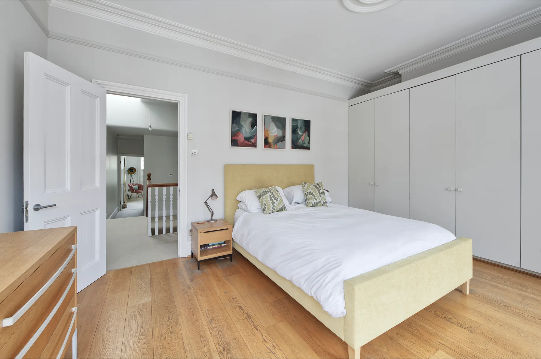 A bright bedroom with a double bed, white wardrobes, and wood flooring.
