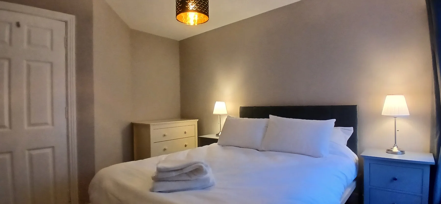 Un dormitorio con una cama grande, mesitas de noche e iluminación cálida.