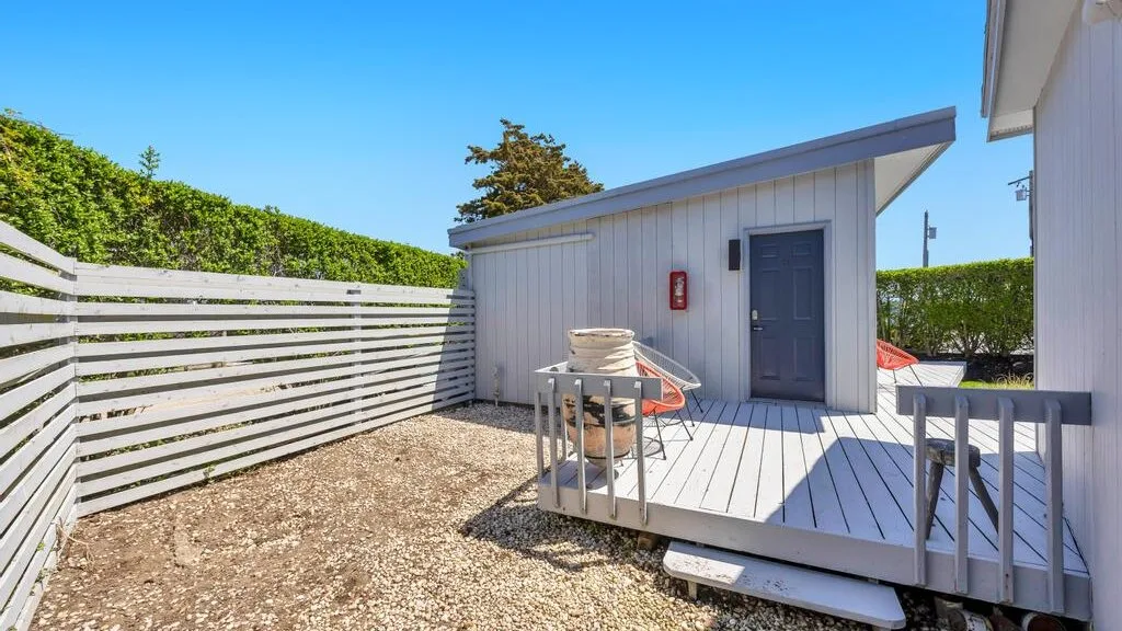 Una pequeña terraza exterior junto a un cobertizo gris, con una mesa y sillas.