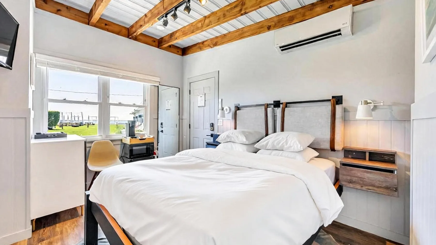Un dormitorio luminoso con una cama tendida y un escritorio junto a la ventana.