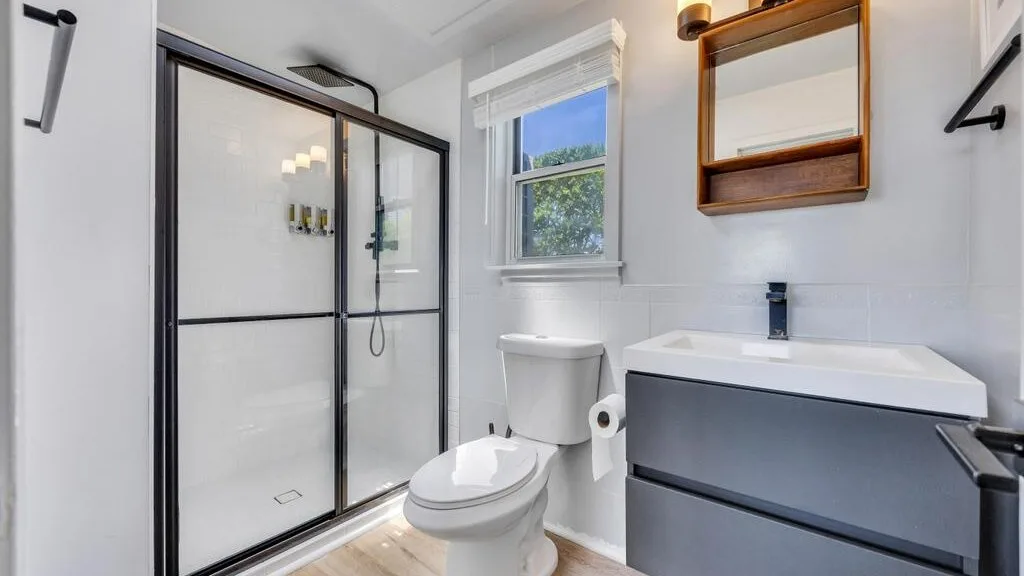 Un baño luminoso con ducha de vidrio, inodoro y lavabo.