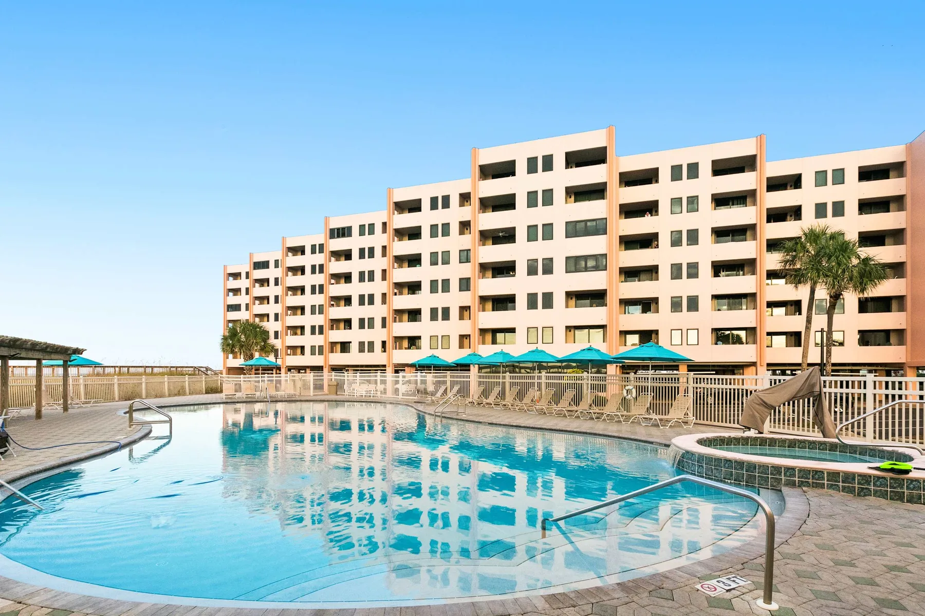 Pool area beside a large multi-story building, with turquoise shade canopies along the deck.