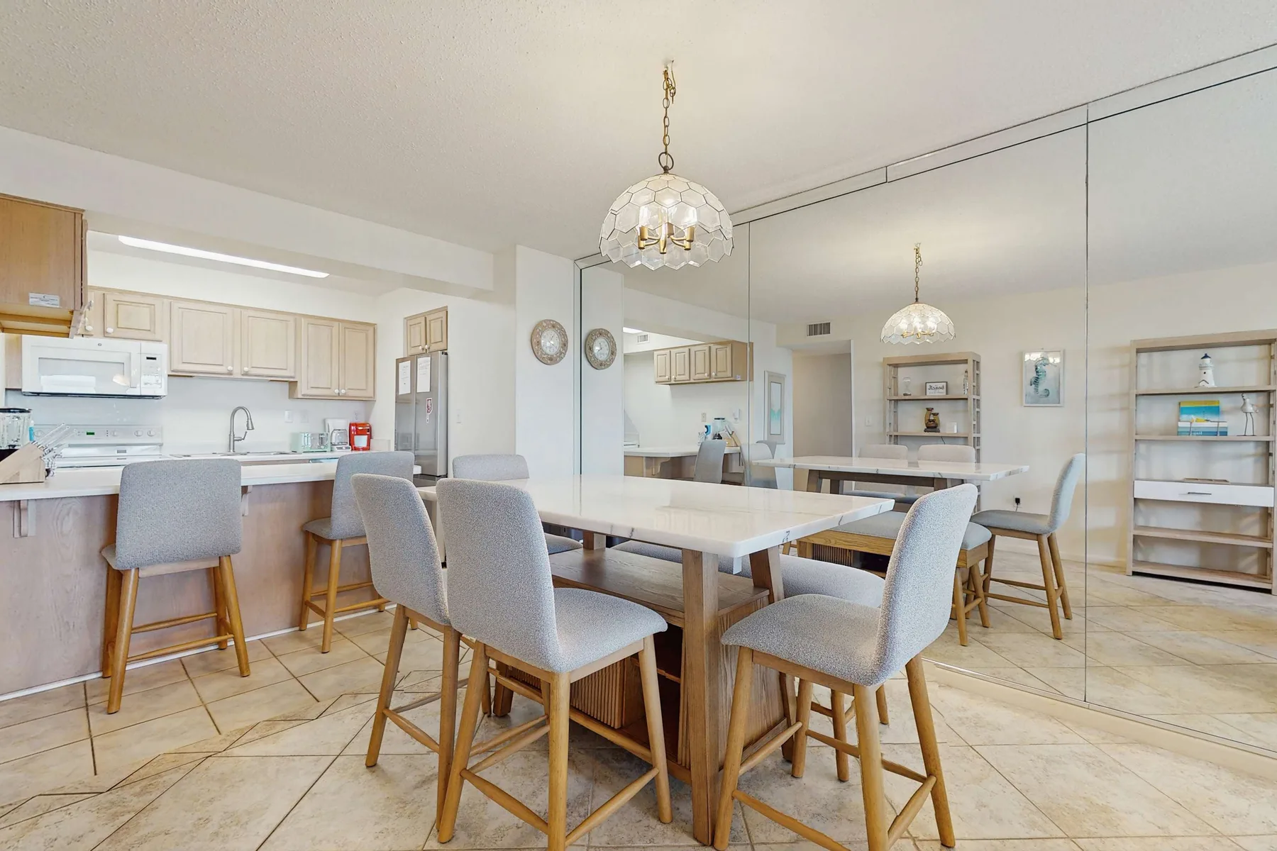 A dining area with a long table and upholstered seating beside an open kitchen.