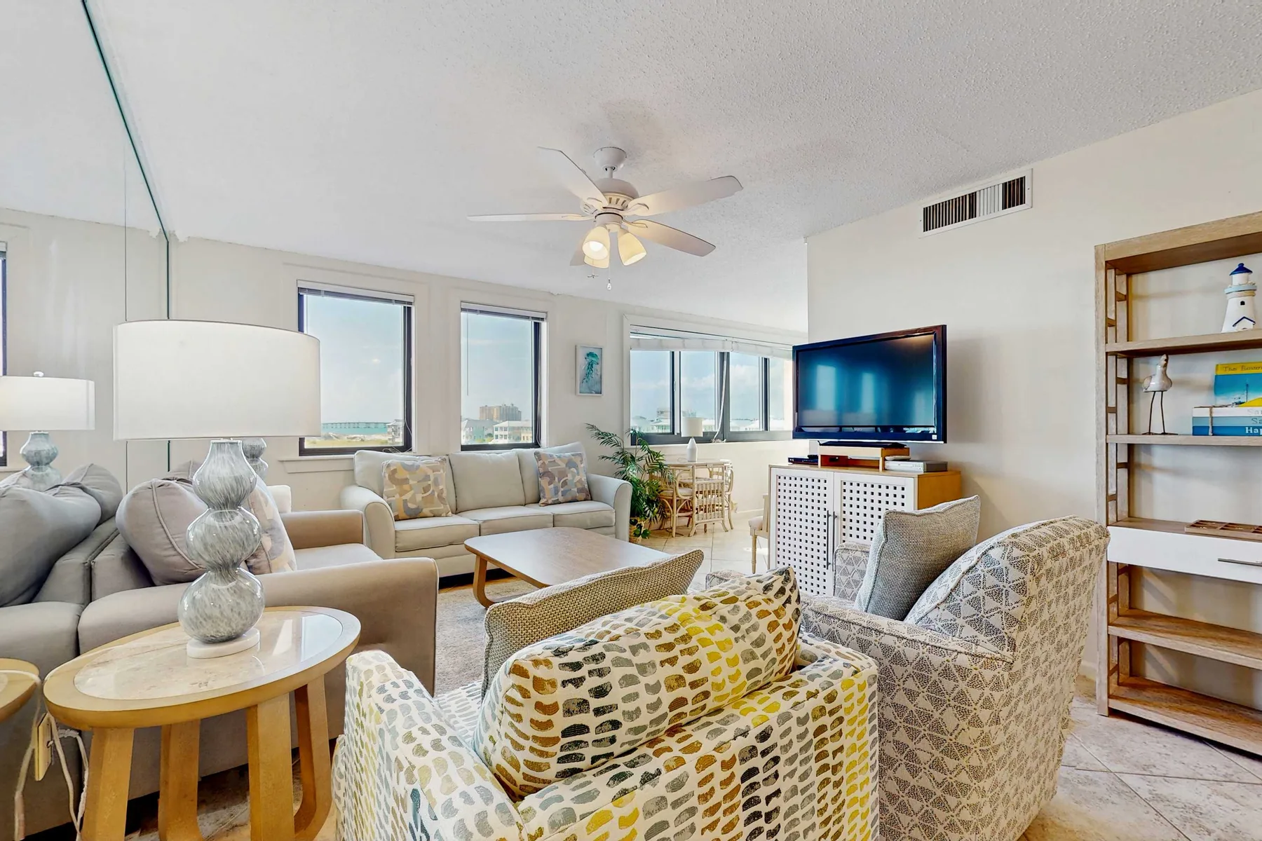 A bright living room with patterned seating, a television, and large windows.