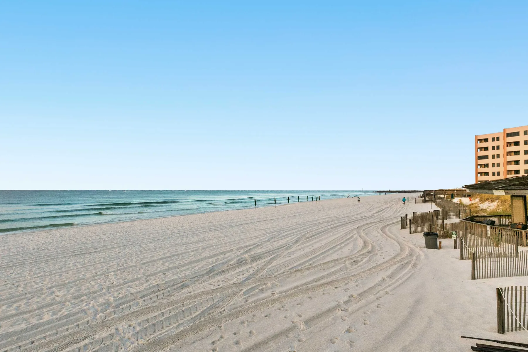 A broad sandy beach stretches beside calm water and beachfront buildings.