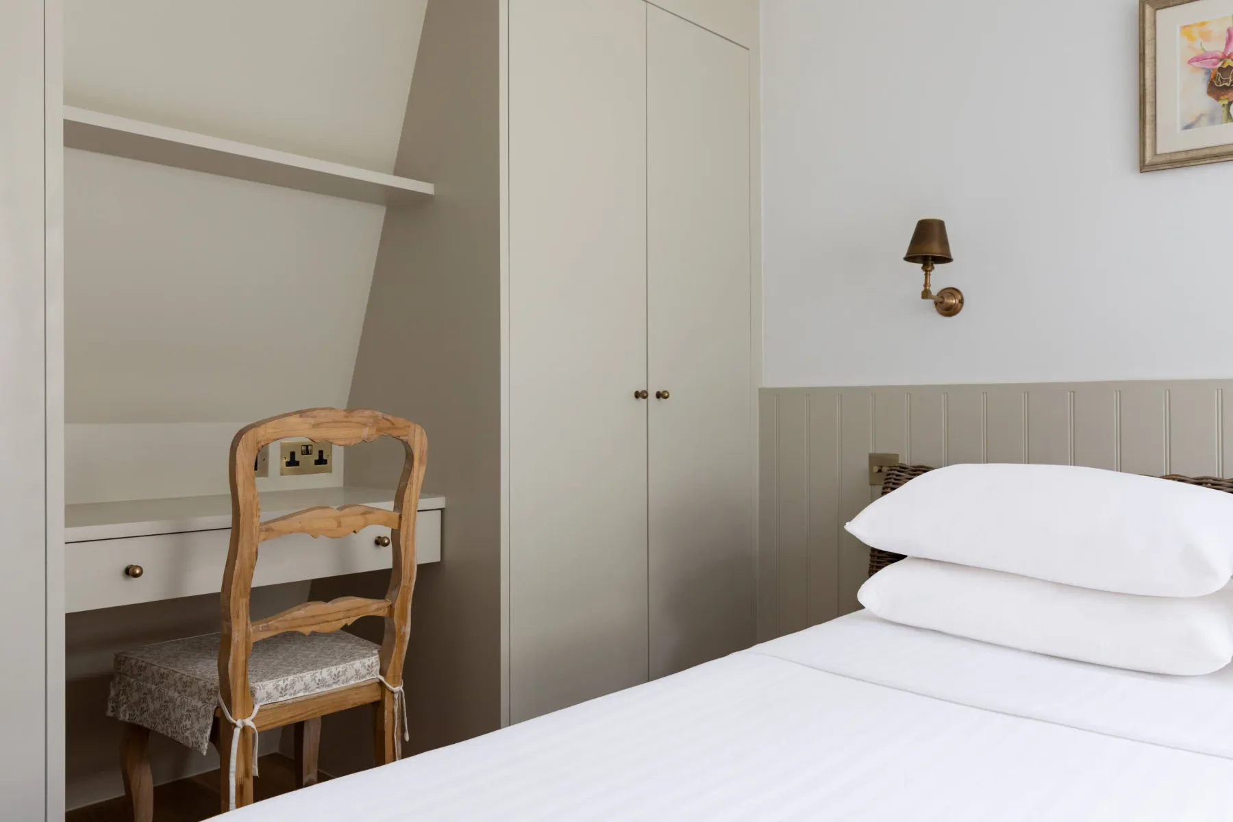 A bedroom with a white bed beside a small writing desk.