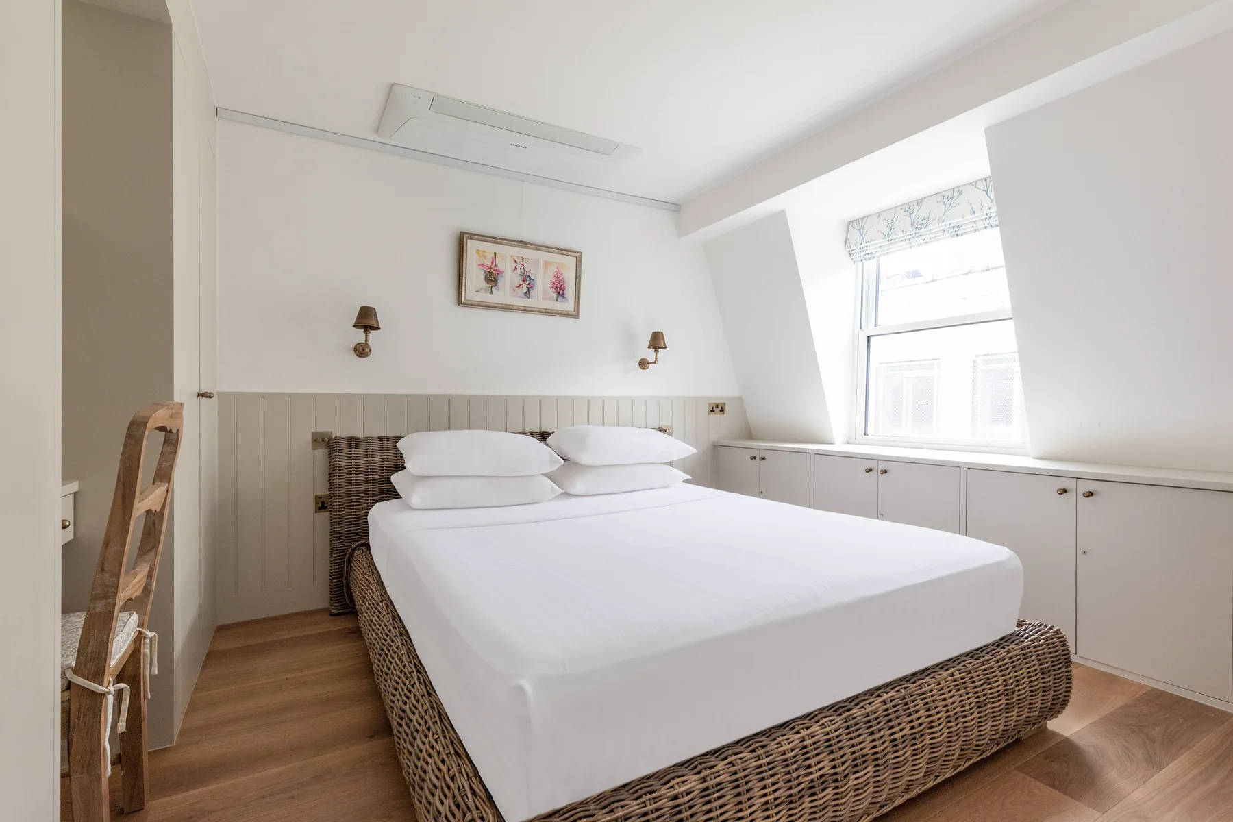 A bright bedroom with a large bed and white cabinets beneath the window.