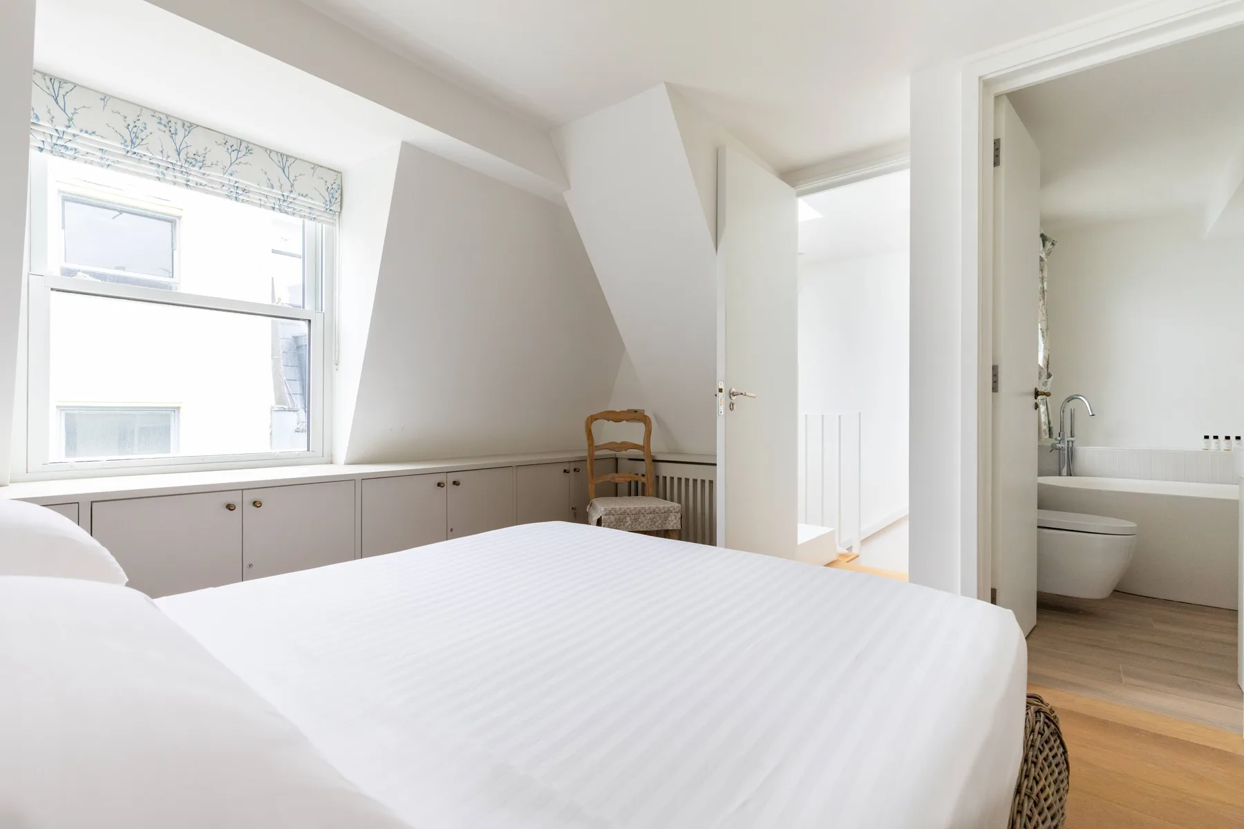 A bright bedroom with a white bed, built-in cabinets, and a window.