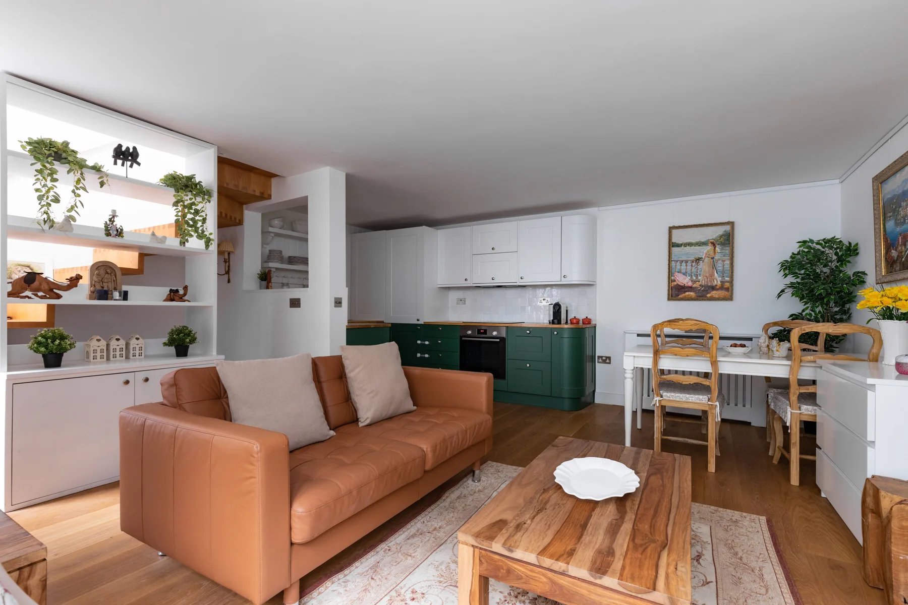 A living and dining area with a brown sofa, wooden table, and white kitchen cabinets.