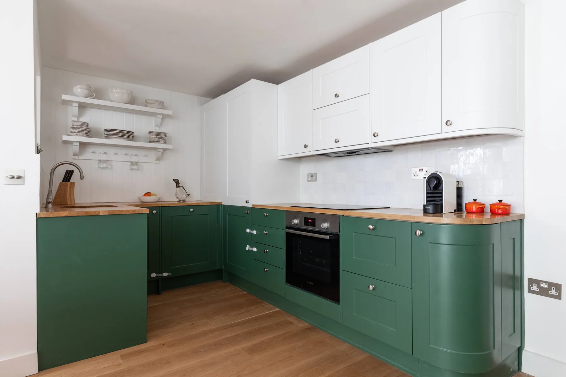 A bright kitchen with green cabinets, white cupboards, and wooden countertops.