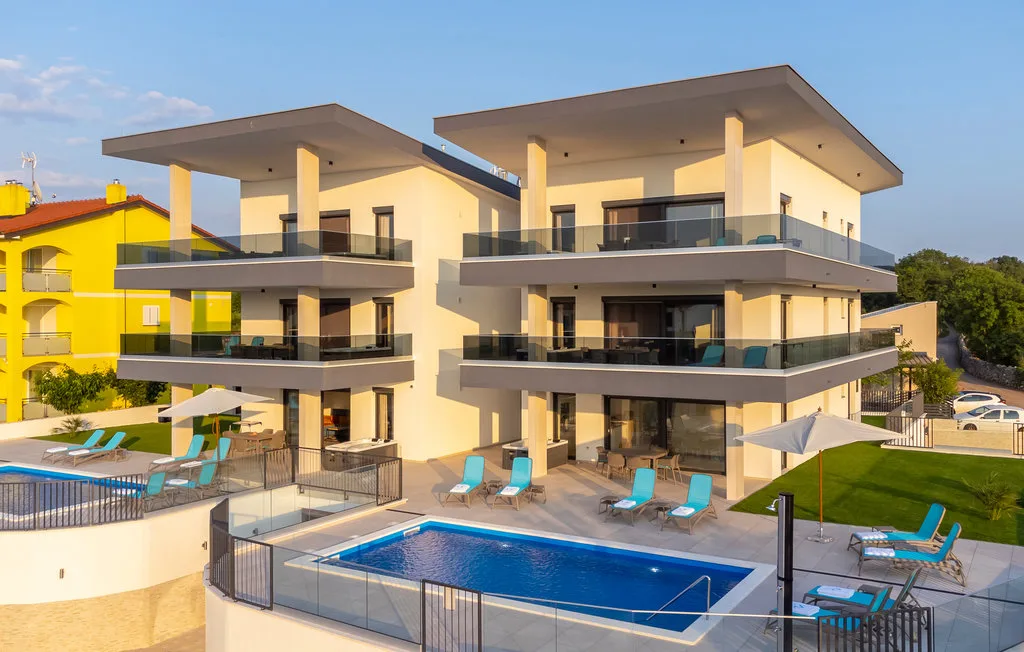A modern apartment building overlooks a swimming pool with lounge seating.