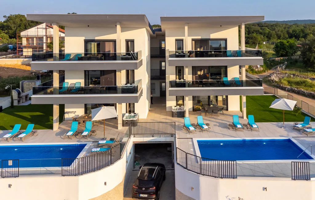 A modern multi-story building overlooks two swimming pools and outdoor seating areas.