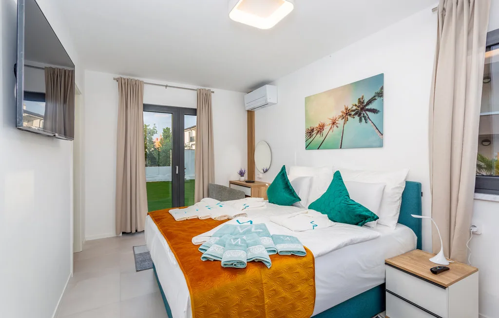 A bright bedroom with a neatly made bed and glass doors opening onto greenery.