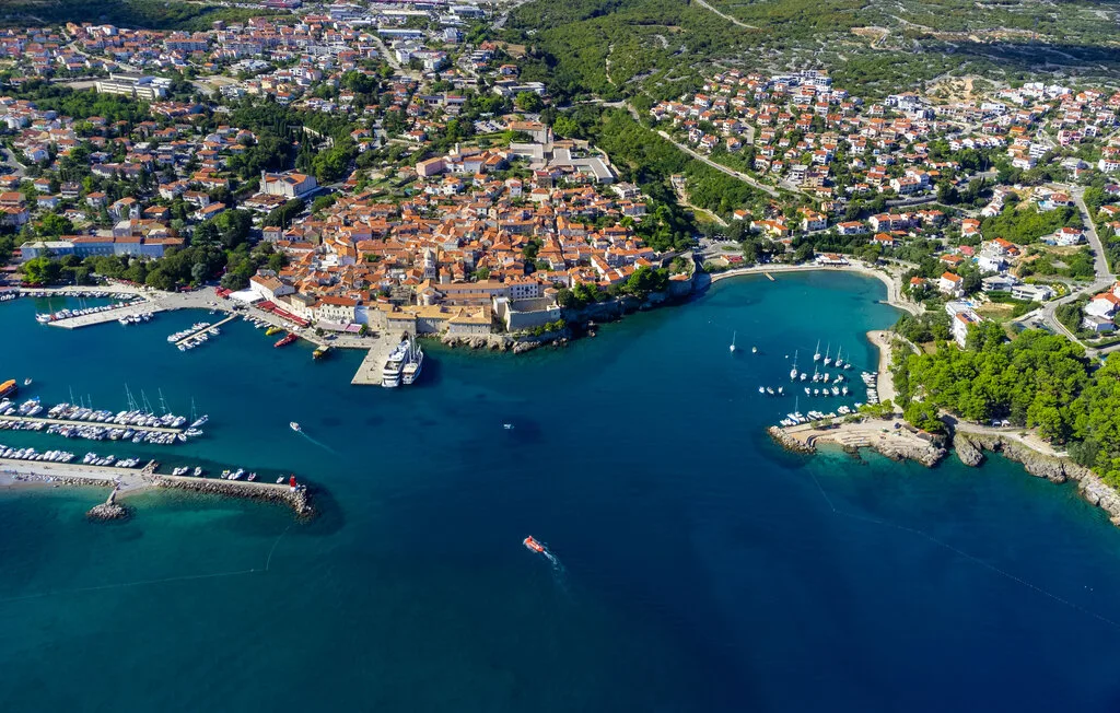 Aerial view of a coastal town surrounding a harbor and turquoise bay.