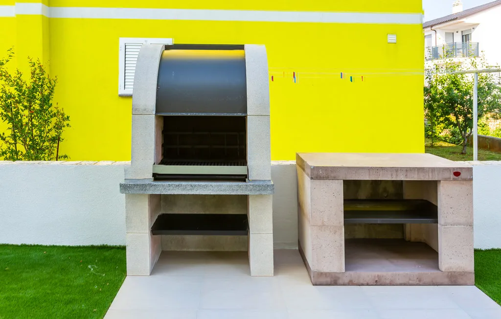 An outdoor cooking area with a built-in grill and stone counter.