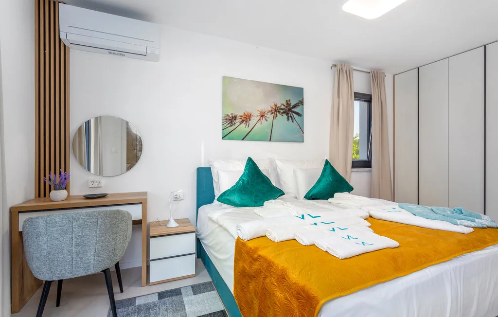 A bright bedroom with a bed, turquoise cushions, and a small desk.