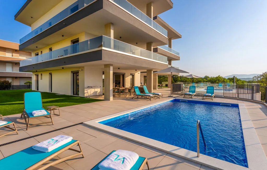 A modern building overlooks a blue swimming pool with lounge seating on the surrounding patio.
