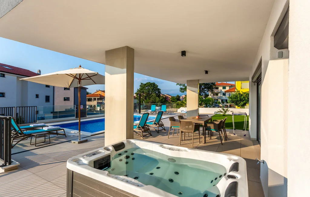 Covered outdoor patio with a hot tub, dining table, and pool view.