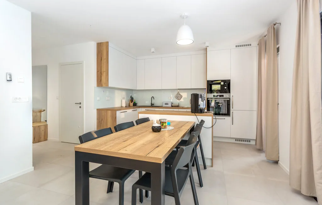 A bright kitchen and dining area with a long wooden table and white cabinets.