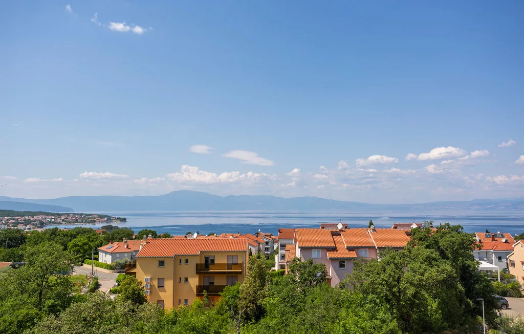 A coastal town with red-roofed buildings overlooks the sea and distant mountains.