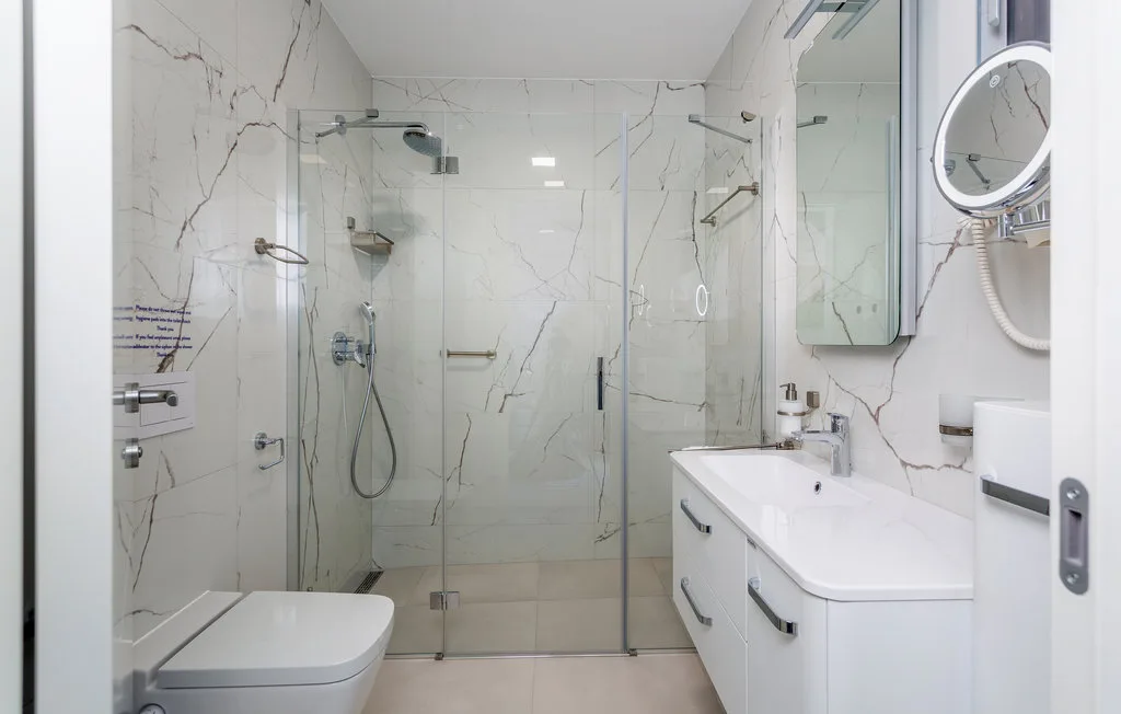 A bright bathroom with a glass shower, toilet, and vanity.