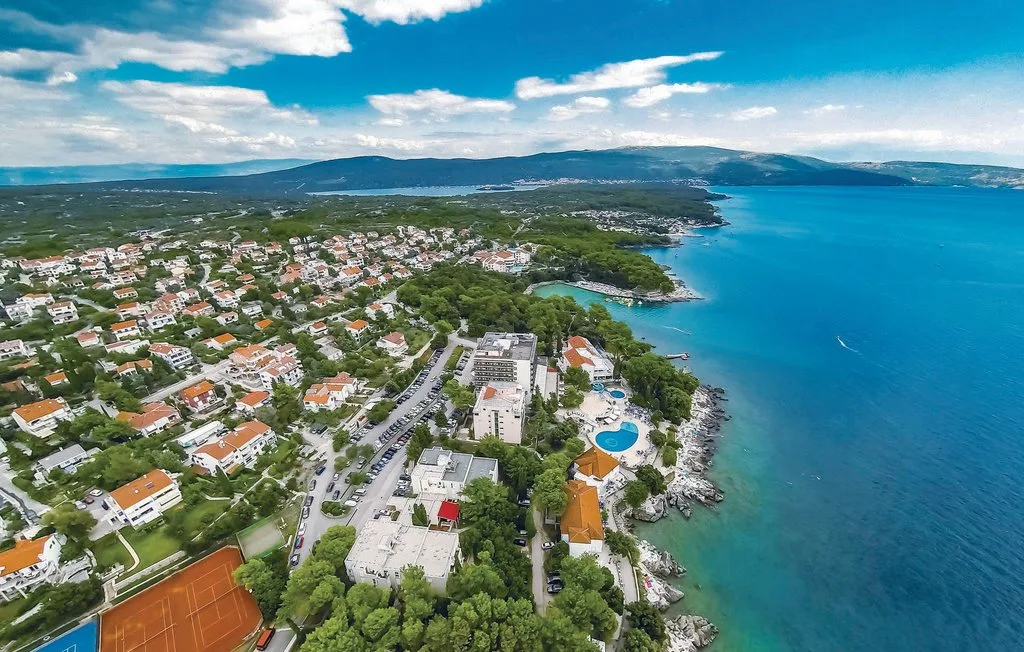 Aerial coastal town scene with buildings, a swimming pool, and blue sea.