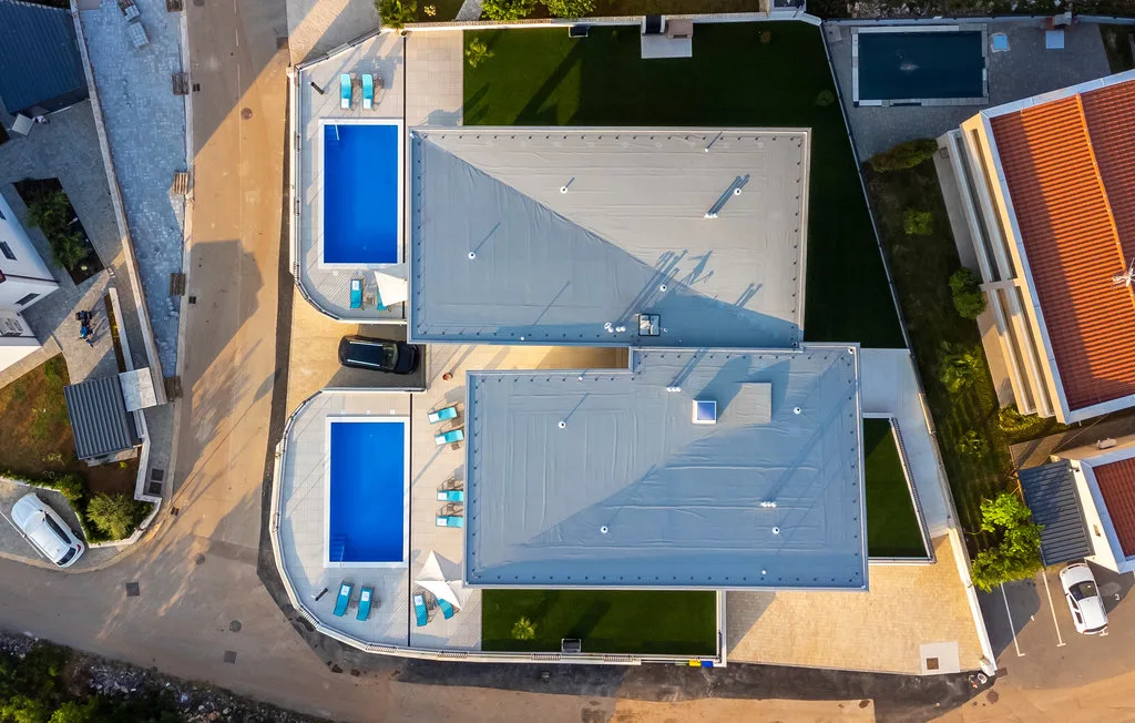 An aerial view of a modern building with two blue pools beside it.