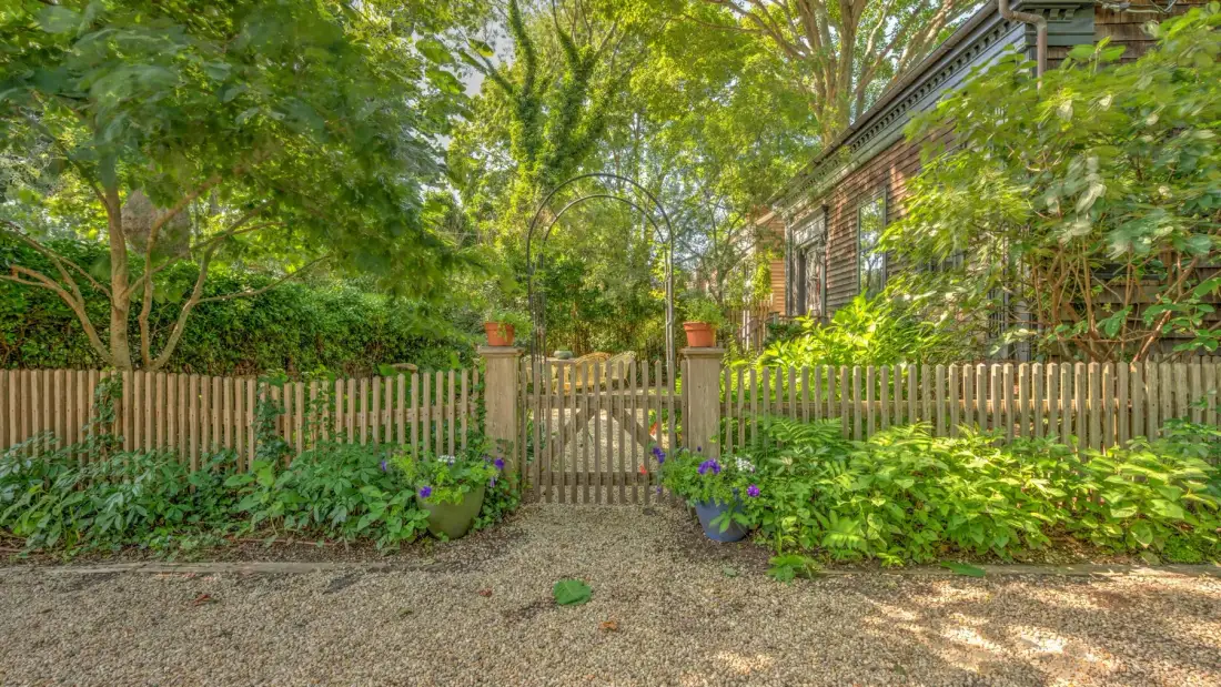 Un sendero de jardín pasa por una puerta de madera junto a una casa de ladrillo.