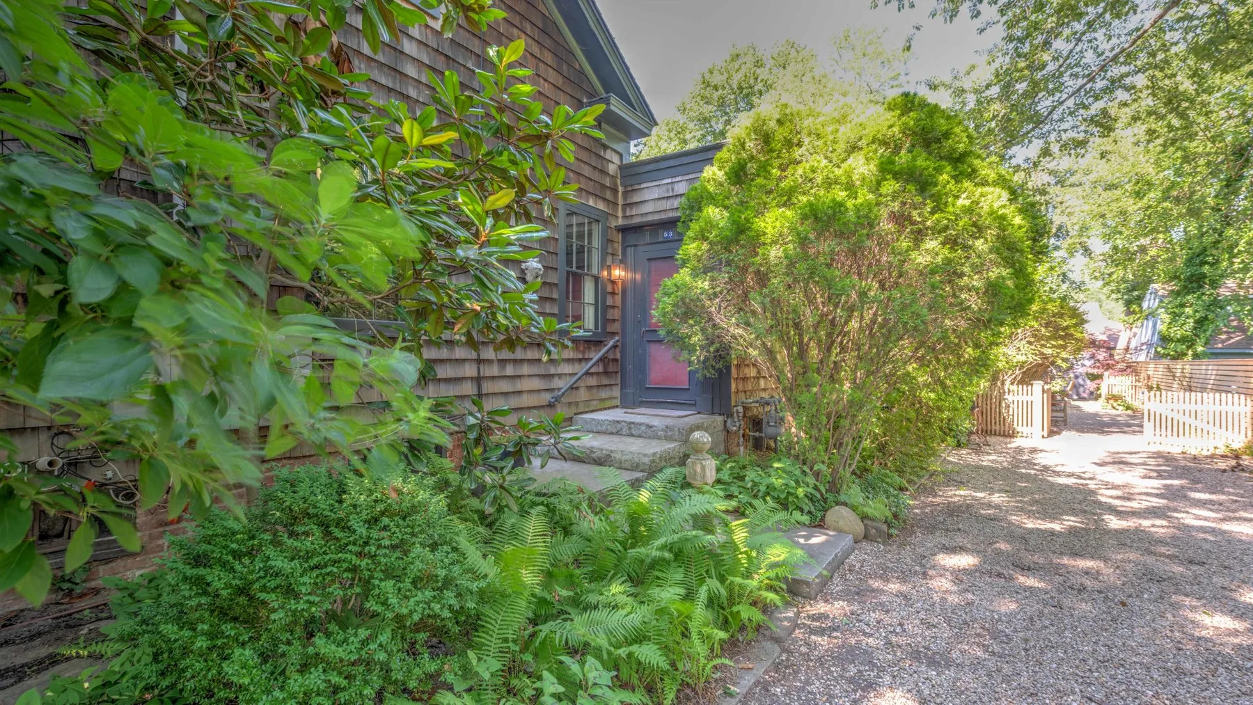 Una entrada de casa frondosa da a un camino de grava junto a plantas de jardín.