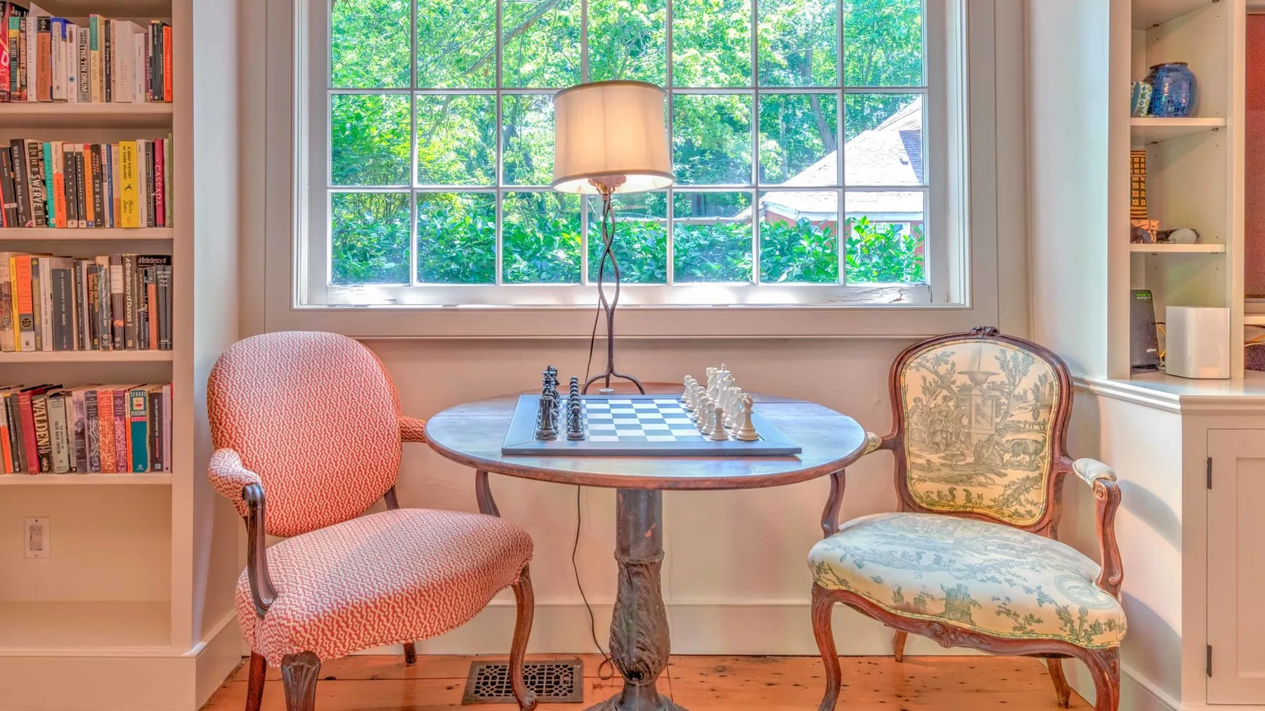 Una zona de estar con una mesa de juego y dos asientos tapizados junto a una gran ventana.
